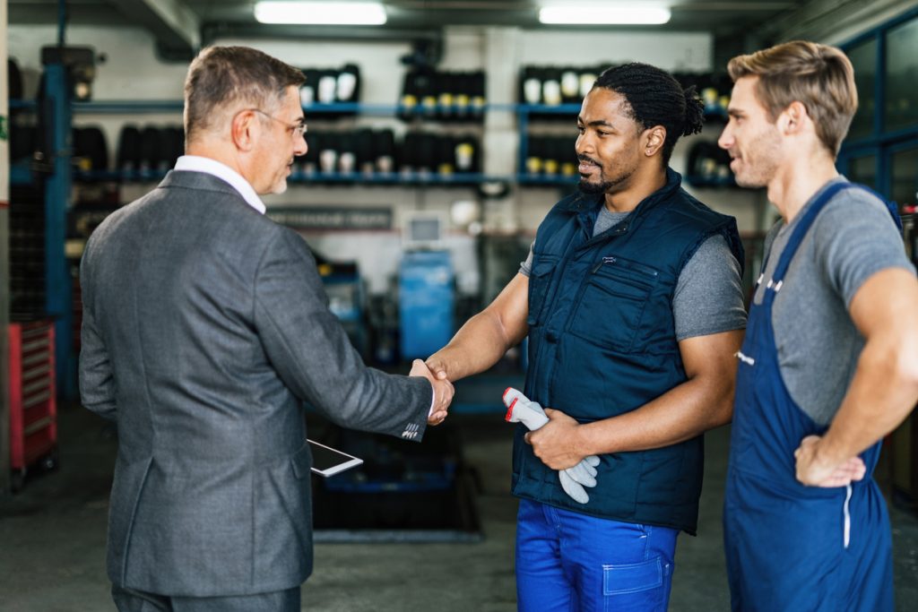 Arbeitgeber-Service, Automechaniker beim Händeschütteln mit seinem Geschäftsführer in der Autowerkstatt