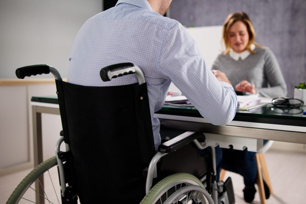 Menschen mit Behinderungen, Mann im Rollstuhl am Schreibtisch